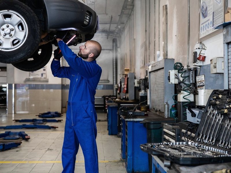 Mechanic inspecting the underside of a vehicle on a lift in a workshop, illustrating a methodical pre-start inspection