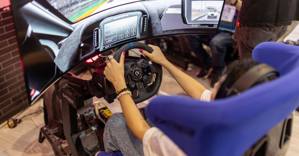 A driver seated in a serious racing simulator cockpit with a force-feedback wheel, pedals and telemetry displays, capturing the screen side of the sim-to-grid journey